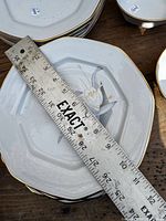 Stack of octagonal plates measured with ruler showing approx 8-inch width, floral motif and gold rim