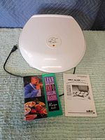 Closed white George Foreman GR30 grill with power cord, owner’s manual and recipe booklet