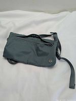Front view showing teal-gray bag, top zipper, lululemon logo badge and part of strap