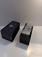 Closed Magic: The Gathering storage box beside full row of trading cards