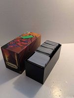 Black storage box filled with MTG cards beside illustrated deck box