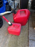 Large and small red plastic gas cans with spouts on driveway