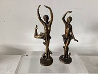 Two bronze ballerina sculptures on clear riser