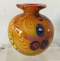 Front view of orange-yellow swirl Murano vase with millefiori medallions