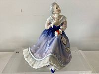Front angled view of figurine showing face, gown colors, gift box and attached tags