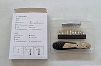 Front view of box with contents list beside plastic tray holding extension, bits on rail, and ratchet handle