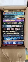 Vertical stack of twelve paperback novels showing titles and authors on spines