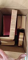 Box containing maroon hardcover volumes, tan dust-jacketed spine visible