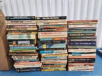 Three tall stacks of vintage mass-market paperbacks on table, spines outward