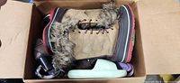 Box with tan faux-fur winter boots on top, mint slide and other footwear partially visible