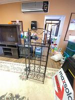 Front view of black wrought iron wine rack showing scroll design and shelves
