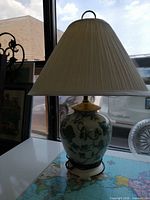 ceramic lamp sitting on table with pleated shade visible