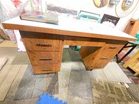Front view of desk showing wood veneer finish, white laminate top, six drawers, center knee space, atlas book on surface