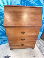 Front view showing drop-front panel and three drawers with brass pulls