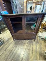 Front view of wood cabinet showing glass doors and drawer