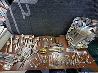 Overview of entire lot showing flatware, souvenir spoons, serving pieces, trivets, vase