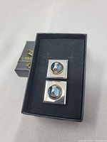 Top view of both cufflinks in box showing square design and blue stones