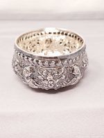 Side view of sterling silver cup showing repoussée decoration and polished rim