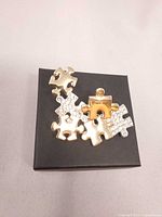 Front view showing gold-tone and rhinestone puzzle design brooch on box