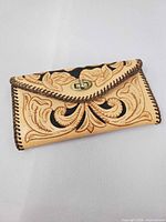 Front view of tan floral tooled leather wallet with braided edge and brass-tone twist lock