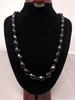 Full view of black faceted bead necklace on display stand