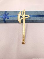 Front view of gold-tone axe brooch on box
