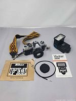 Full kit laid out: camera with lens, flash, manuals, strap, cable release, lens cap