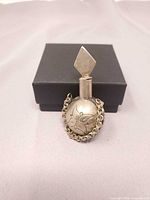 Perfume vial upright in front of box showing butterfly engraving and chain