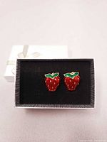 Front view of both strawberry clip-on earrings in box