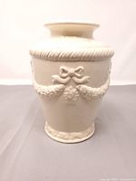 Front view of white ceramic vase showing raised bow and floral swag