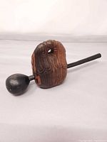 Full view of carved wooden instrument resting on side with mallet attached