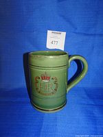 Front view of green Denby coronation mug displaying crest