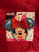 Front of packaged Minnie sequined headband showing ear, bow, flower and branding