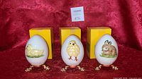 Three Goebel eggs with stands and boxes