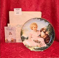 Front of plate with girl and dog artwork next to box and certificate