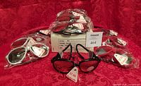 Box with multiple packaged sunglasses: black, red, white; central pair displayed