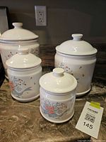 Four white porcelain floral canisters with lids on countertop