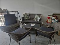 Full view of wicker loveseat, one armchair, ottoman, coffee table, cushions, and pillows