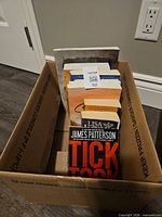 Box containing visible paperbacks headed by Tick Tock by James Patterson, additional titles behind