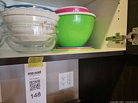 Group of bowls in cabinet: ceramic floral bowl nested in glass, green plastic bowl on plastic plates