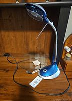 Full view of blue and silver LED gooseneck desk lamp with cord and plug