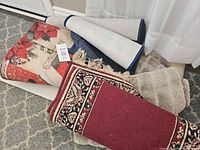 Pile of rolled rugs showing burgundy runner, gray shag, holiday rug and others