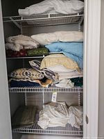 Overview of closet shelves showing assorted pillows, comforters, blankets and sheet sets