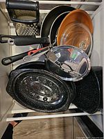 Drawer view of mixed cookware set including pans, lids, enamel roasters, grater, tongs