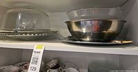 Shelf view showing glass cake dome on matching plate, nested bowls, and metal tray