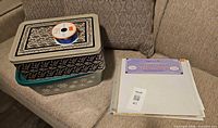 Metal tin with ribbon spool on top and plastic storage tub, shown on couch