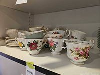 multiple floral porcelain teacups stacked with saucers visible