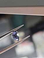Pear-cut purple spinel held by tweezers, side view