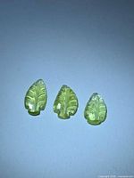 Three lemon-lime leaf-cut tourmaline gemstones on neutral background