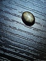 Oval black star sapphire showing asterism on textured surface